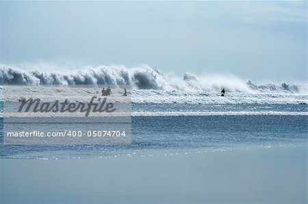 surfers silhouetted against crashing waves, kuta beach, bali