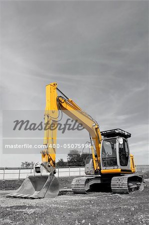 Industrial yellow digger with excavator bucket standing idle on a building site. Desuaturated with only the metal on the vehicle saturated.