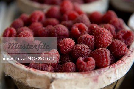 A close-up image of baskets filled with ripe red raspberries