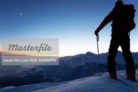 At dusk a brave backcountry skier reaching the summit of the mountain after a long day walking in the wilderness. Adventure and exploration concept.