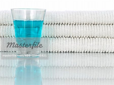 A glass full of mouthwash on a background of clean and white towels.