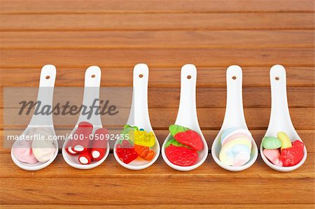 Assortment of candies in the spoons with soft shadow in the wooden background