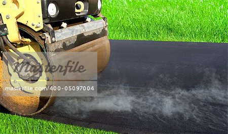 Road roller leveling fresh asphalt pavement on the green grass