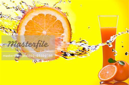 View of piece of orange getting splashed  and  glass of juice on back
