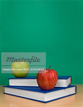 A blank chalkboard with apples over books.