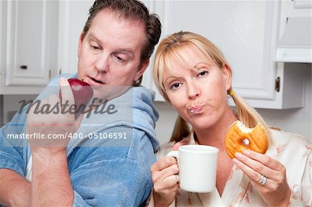 Couple in Kitchen Eating Donut and Coffee or Healthy Fruit.