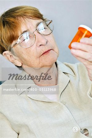 Elderly woman reading pill bottle label with glasses