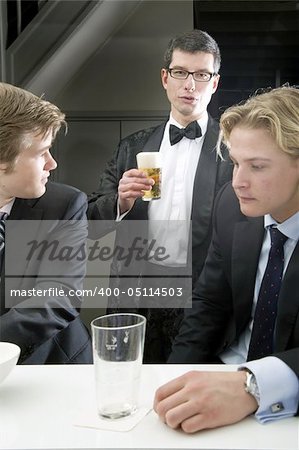 three men drinking a beer at a bar in fashionable outfits