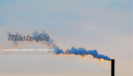 The smoke from a pipe is illuminated by the sun at sunset