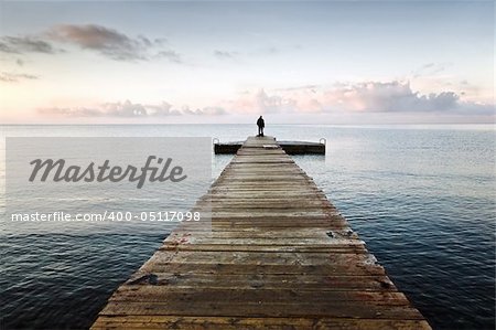 Lonely silhouette standing on an empty wooden pier in the morning with beautiful clouds and azure sky
