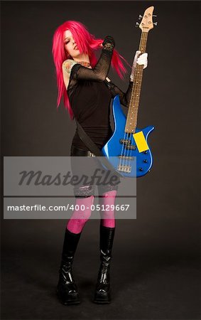 Attractive girl putting on bass guitar, studio shot on black background