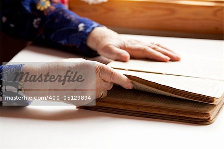 An old pair of hands holding the pages in a book, reading.