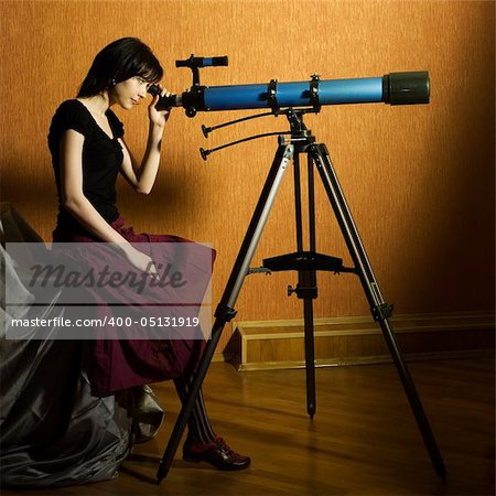 Young beautiful girl sitting on the bed looking to the telescope
