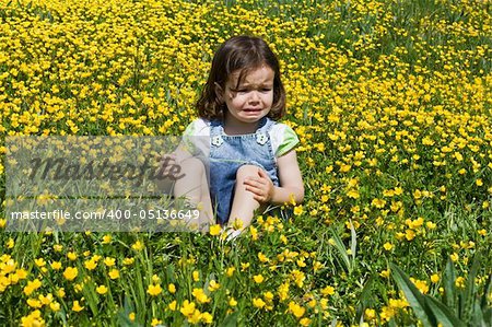 Crying girl sitting on a meadow full of buttercup