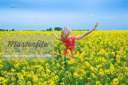 happy blond girl with open arms to the sky smilimg in a yellow field