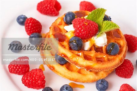 Belgian waffles with fresh strawberries, blueberries, mint leaves and cream on white plate