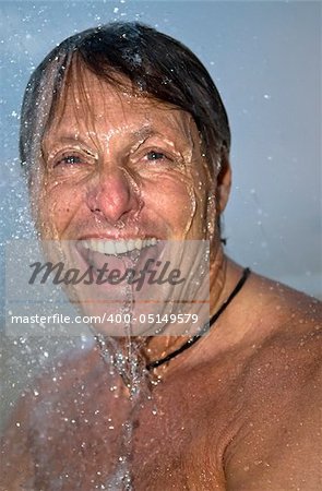 handsome forties man is laughing as he has fun under a powerful shower.