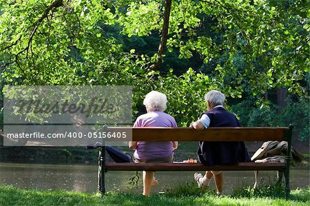 Aged couple enjoy spring morning on the bench near lake in the park