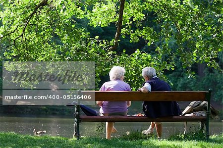 Grandparents are sitting on the bench and talking to each other in the spring park