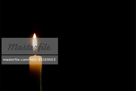 a single tall lit candle on a black background isolated