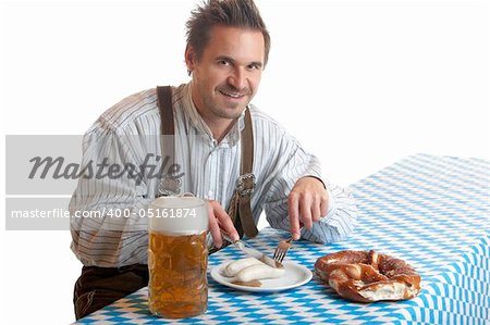 Bavarian Guy is sitting at table and having a typical Oktoberfest meal with pretze (Brezn), veil sausage (Weisswurst), beer at beer stein (Mass). Isolated on white background.