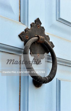 An old weathered door knocker from a light blue painted wooden door