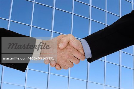 Two caucasian businessman in a black business suits shaking hands to close a deal. They are shown in front of an office building