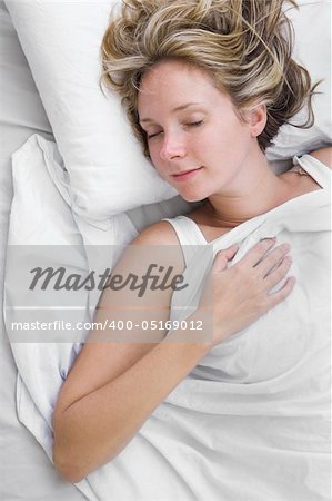 Woman asleep in bed wrapped in white sheets