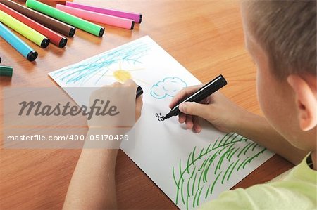 child draws green grass and sun on white paper by colour pensil