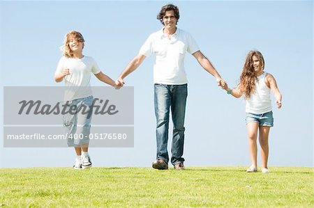 Daddy having fun with his children on meadow as he walks holding their hands