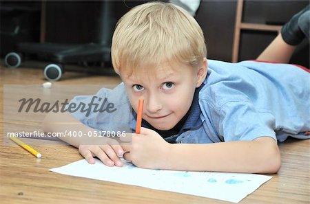little boy drawing using  pencils, he is laying on the flour