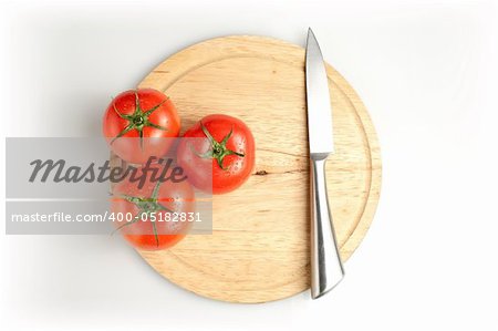 Three tomatos and stainless knife on wood plate