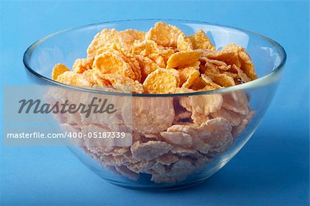 Small portion of cornflakes in the little glass bowl over blue background