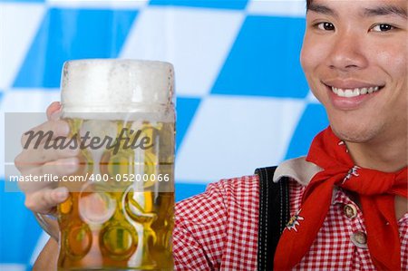 Asian Boy is holding a full Oktoberfest beer stein and smiles happy in camera. Isolated on white.