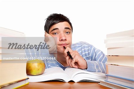 Young handsome student sitting on a desk between study books and looks frustrated. Isolated on white.