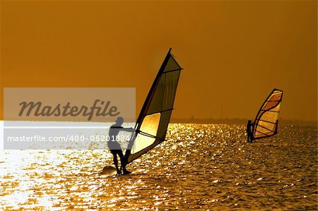 Silhouettes of two windsurfers at the sunset