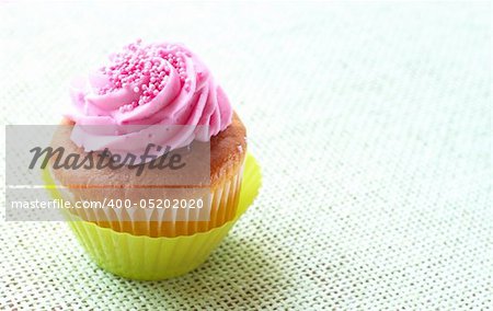 Small vanilla cupcake with strawberry icing on green mesh background