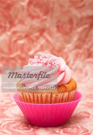 Fresh vanilla cupcake in pink cup with strawberry icing and sprinkles on decorative background