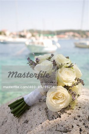 Wedding bouquet on a stone wall with boats and water in the background.