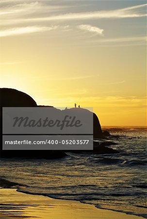 Three people fishing at sunset on a cliff at Clifton, South Africa.