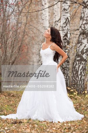 Young brunette in a wedding dress standing in an autumn forest