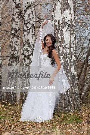 Young brunette in a wedding dress standing in an autumn forest