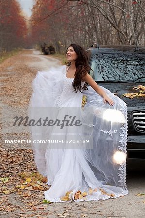 Young woman in a wedding dress standing near the jeep in an autumn forest