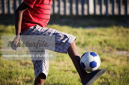A teenage boy with only his legs in shot holding a soccer ball up with just his feet