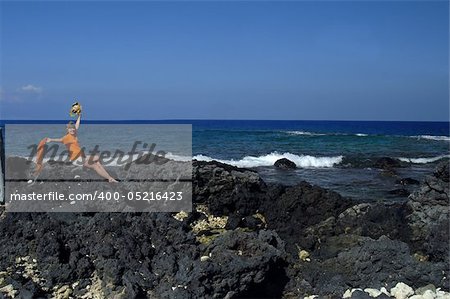 Older woman celebrates retirement and waves while sitting on one of the black lava beaches on the Big Island of Hawaii.