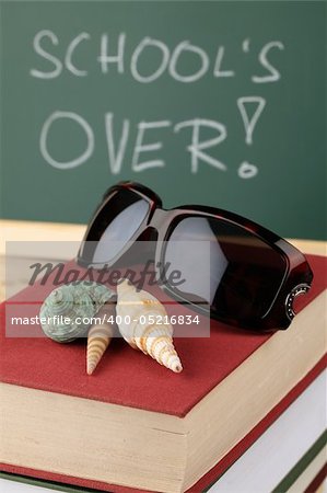 Sea shells and sunglasses on a pile of books and a chalkboard in background with text: School is over