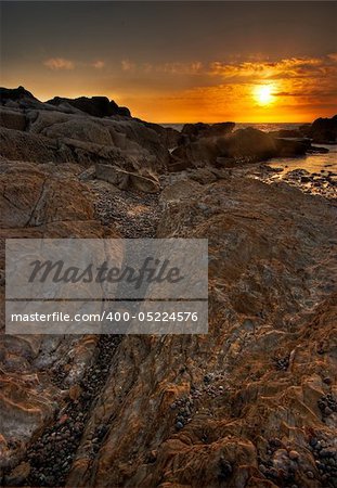 A vertical shot showing the rocky details along the beach with the sun setting over the Pacific Ocean