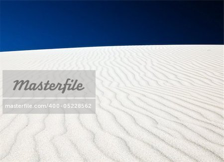 White sand dune with wind patterns and bright blue sky