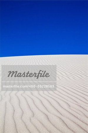 White sand dune with wind patterns and bright blue sky