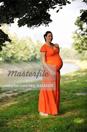 beautiful young happy pregnant woman outdoor in bright nature in orange dress